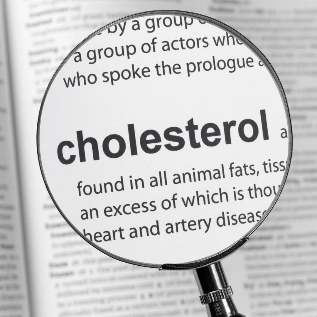 Magnifying glass focusing on the word cholesterol in a dictionary or book.