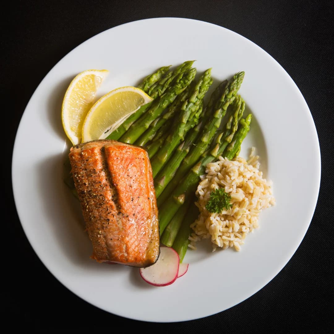 Grilled salmon served with steamed asparagus, brown rice, and lemon wedges on a white plate