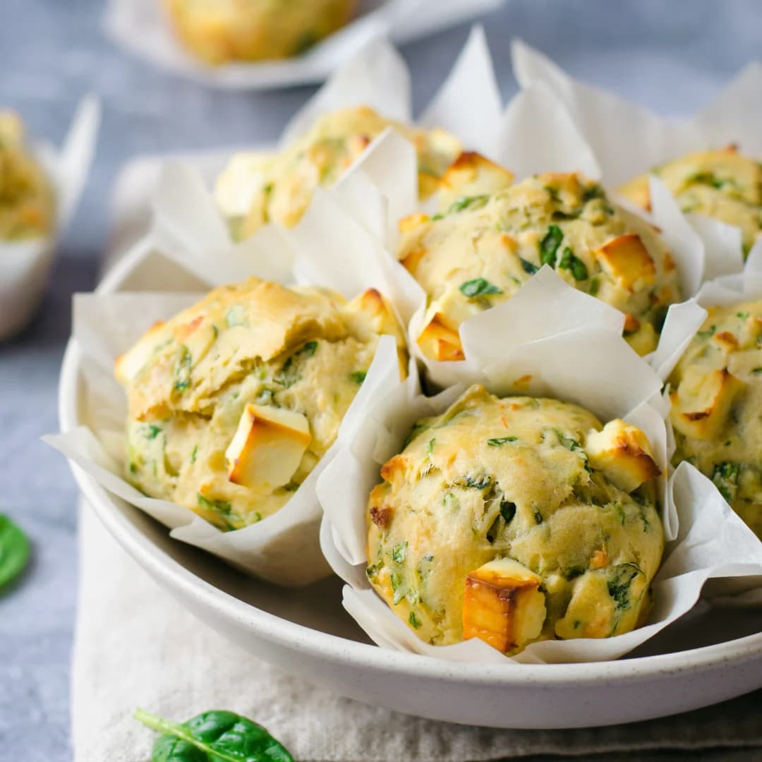 Savory spinach and feta muffins served in white parchment paper cups on a ceramic plate.