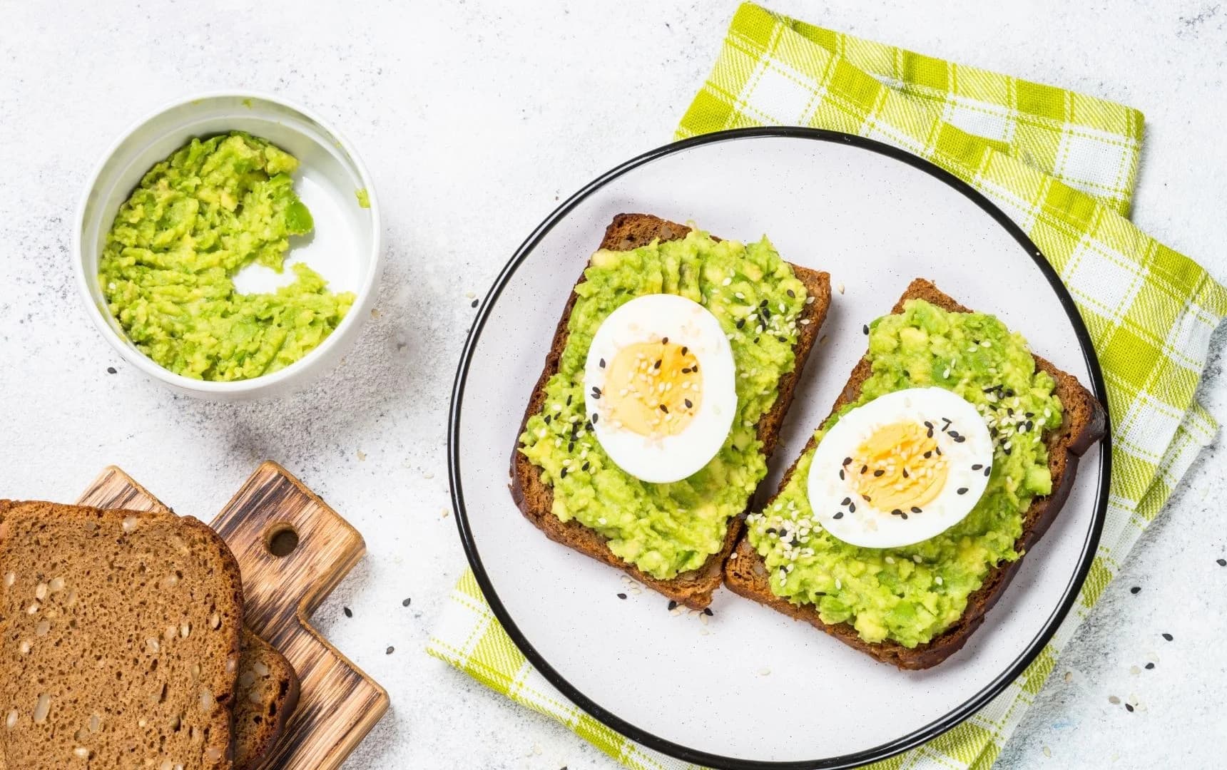 Brown bread toast topped with mashed avocado and sliced boiled egg served on a white plate