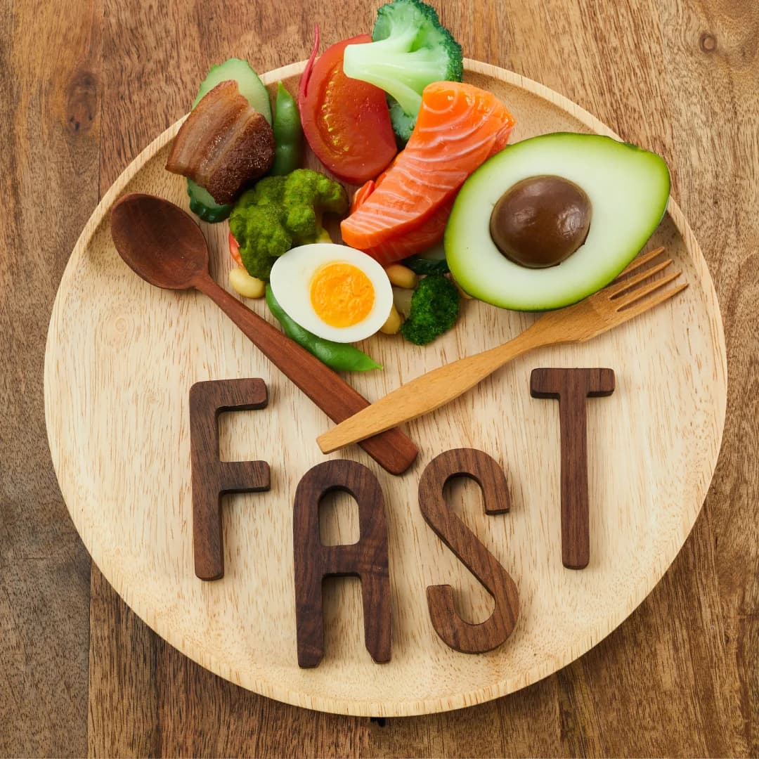 Top view of a wooden plate with healthy foods like salmon, avocado, boiled egg, vegetables, and wooden utensils, with the word FAST spelled out in wooden