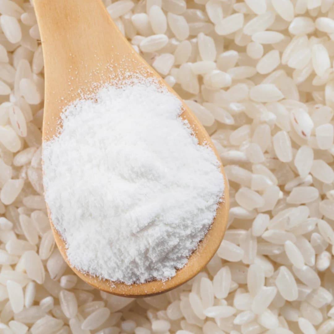 Organic rice flour on wooden spoon with raw white rice grains background