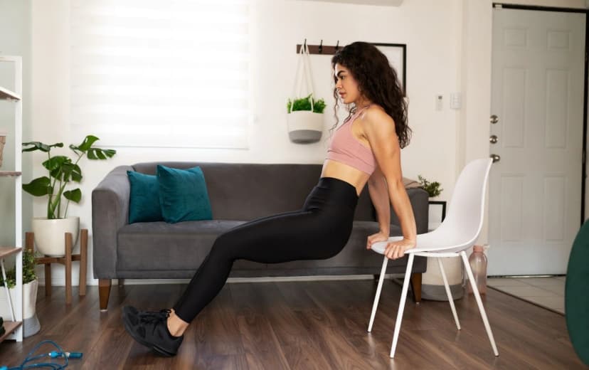 Female doing tricep dips exercise with chair support during home workout
