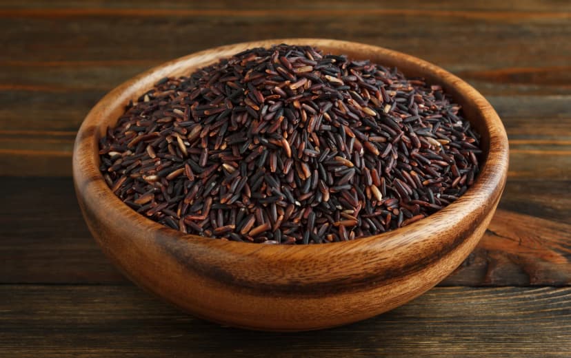 front view black rice in the wooden bowl placed in the wooden table