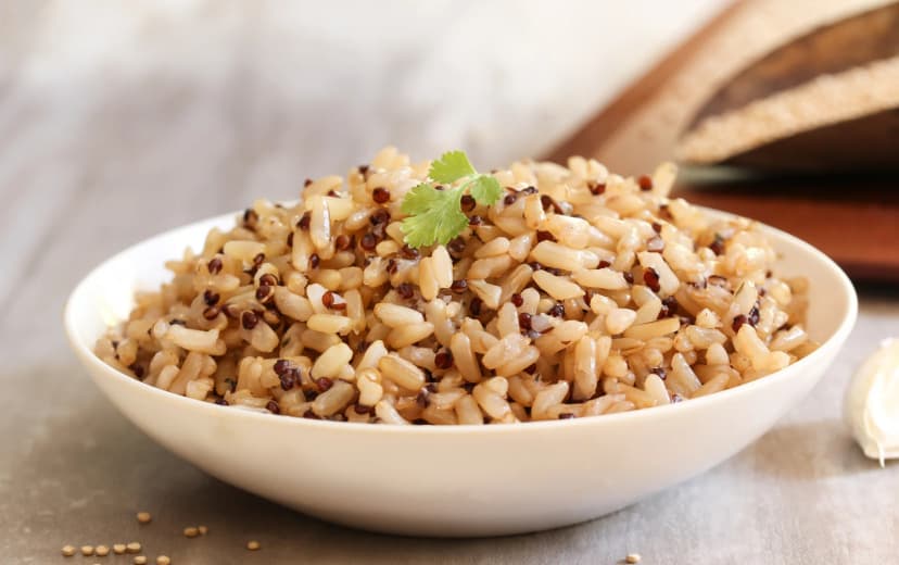 front view of coocked brown rice served in the white bowl placed in wooden table