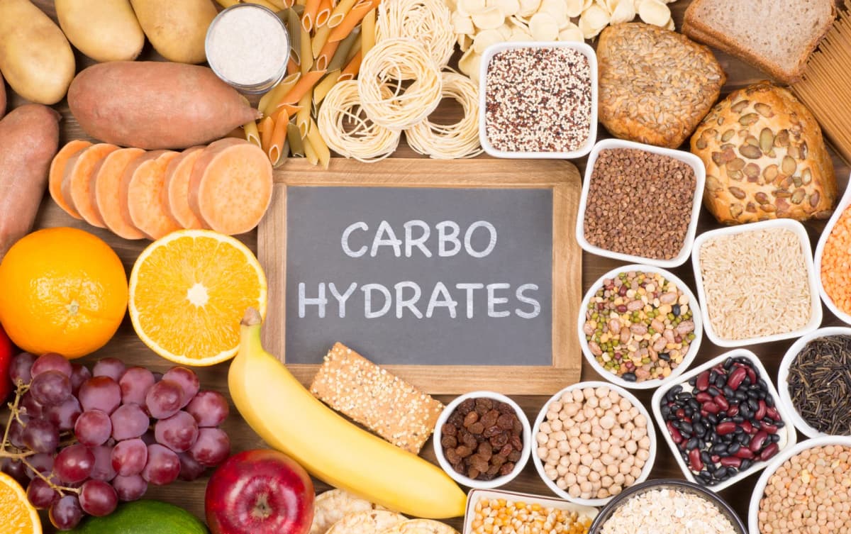 Wide variety of complex carbohydrates including legumes, grains, fruits, vegetables, and pasta with a chalkboard labeled CARBOHYDRATES