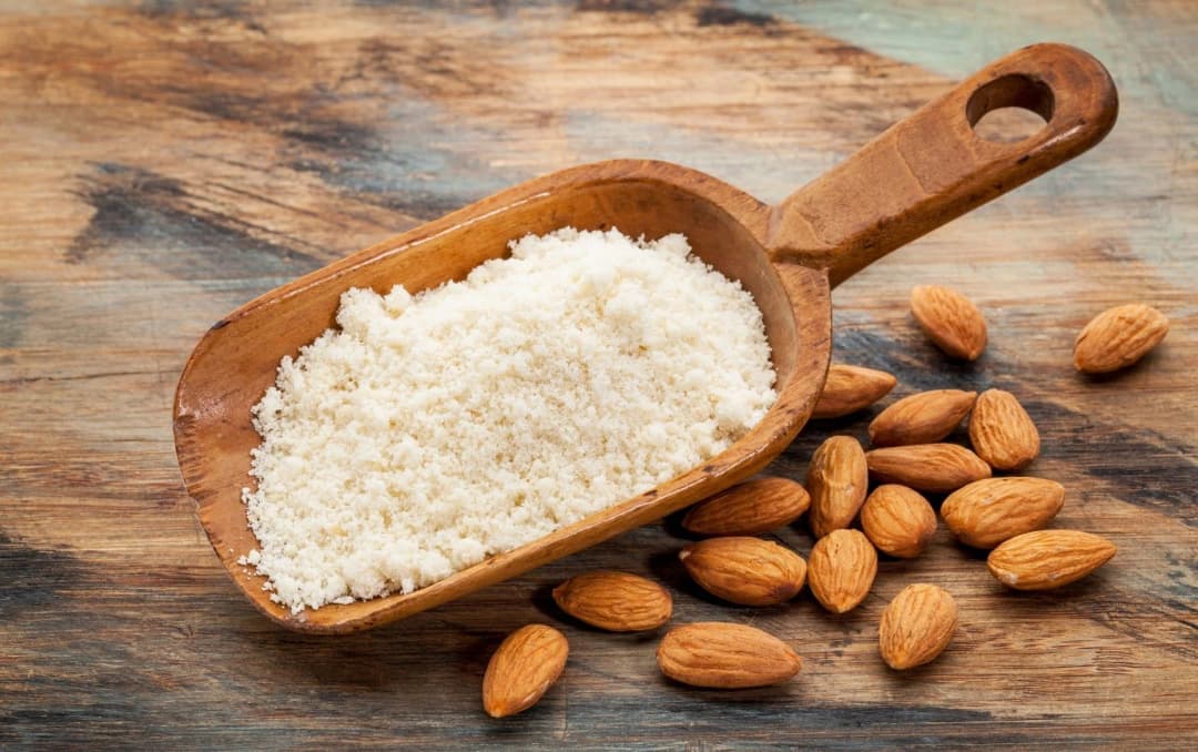 Organic almond flour in scoop with whole almonds on wooden background