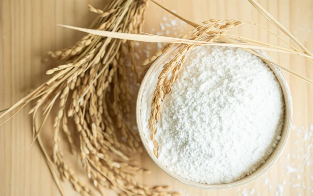 Organic rice flour in a bowl with rice grains on wooden background