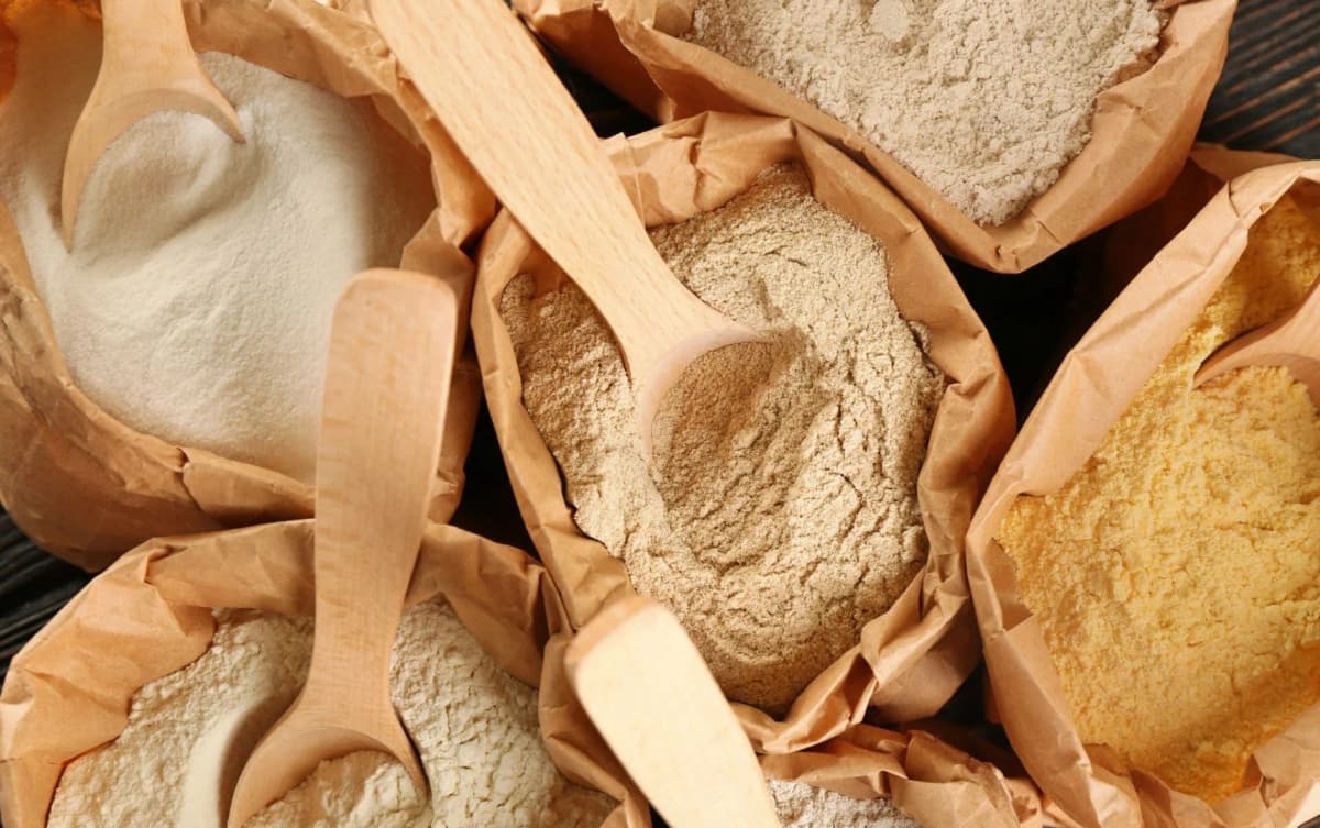 Different types of flour in brown paper pouches with wooden spoons