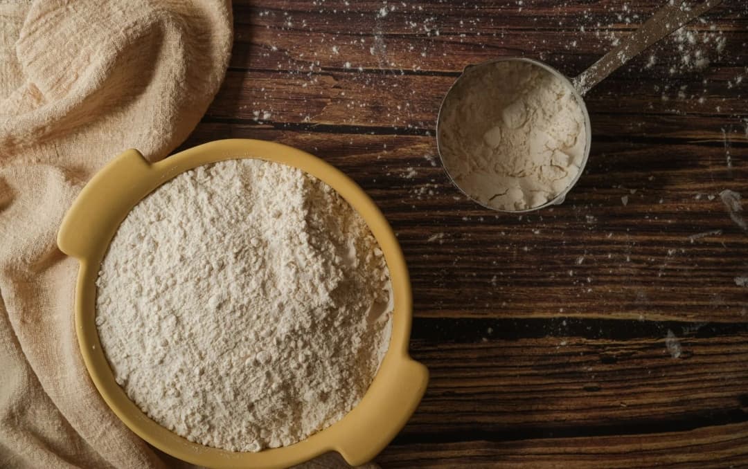 top view of refind wheat flour in the plastic bowl placed on wooden table