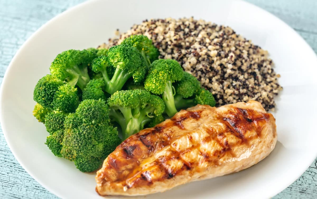 Grilled chicken breast served with steamed broccoli and a portion of quinoa on a white plate