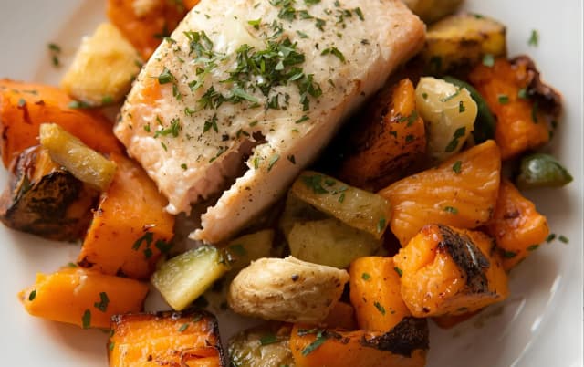 Oven-baked white fish fillet topped with herbs, served with roasted sweet potatoes, zucchini, and root vegetables