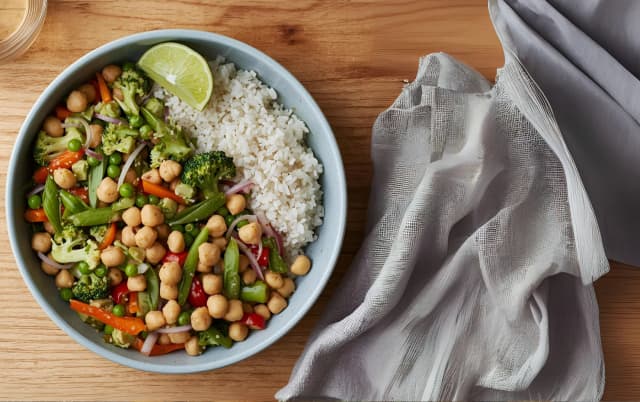 Vegan chickpea salad bowl with white rice, broccoli, snap peas, and colorful vegetables garnished with a lime wedge