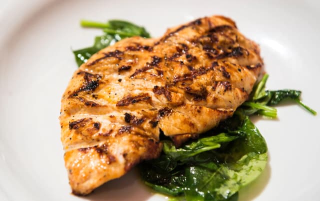 grilled chicken breast top on the spinach leaves served in white plate