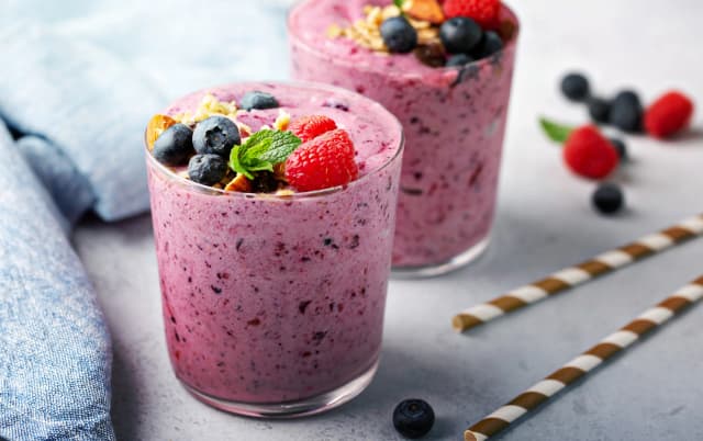 Two berry smoothies in clear glasses topped with raspberries, blueberries, granola, and mint.