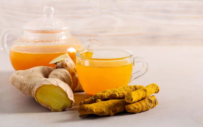 front view of ginger and turmeric tea on the table with tea pot full of tea