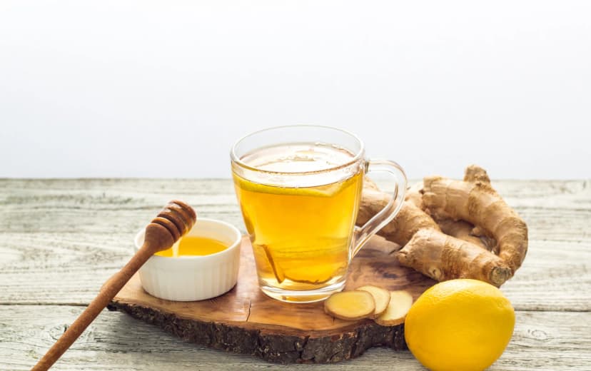 front view of lemon and honey tea served in glass cup ginger and lemon. honey in dip and honey spoon in background placed in wooden board
