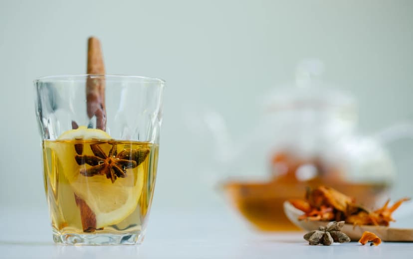 front view of lemon tea also clove and lemon cinnamon stick on the cup cinnamon stick and cloves, glass kettle in the background