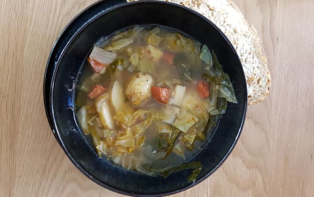 top view of cabbage soup onion, tomatos inside served in black bowl placed in wooden table