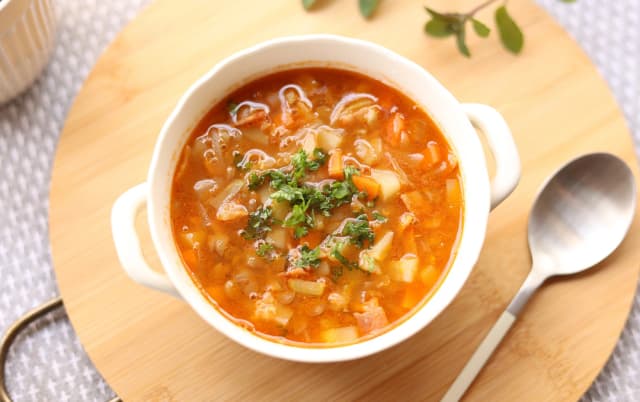 top view of lentil soup tomato and onion inside spinich for garneshed served in white soup bowl place in cercle wooeden board