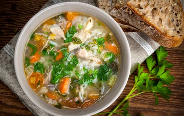 top view of vegitable soup spinich , carrot, tomato inside served in white bowl curriander and brown toast on the background place on the rastic clothe on the wooden table