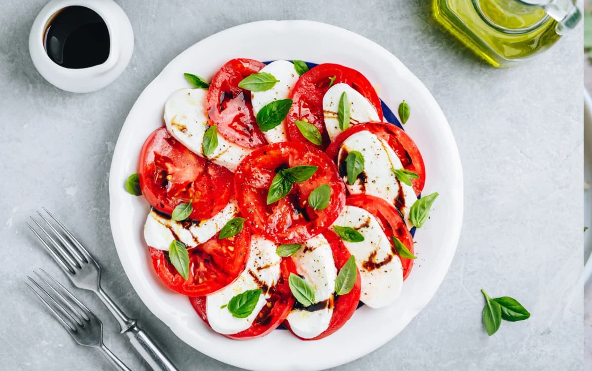 Classic Caprese salad on a white plate with alternating slices of fresh tomato and mozzarella, topped with basil leaves and drizzled with balsami