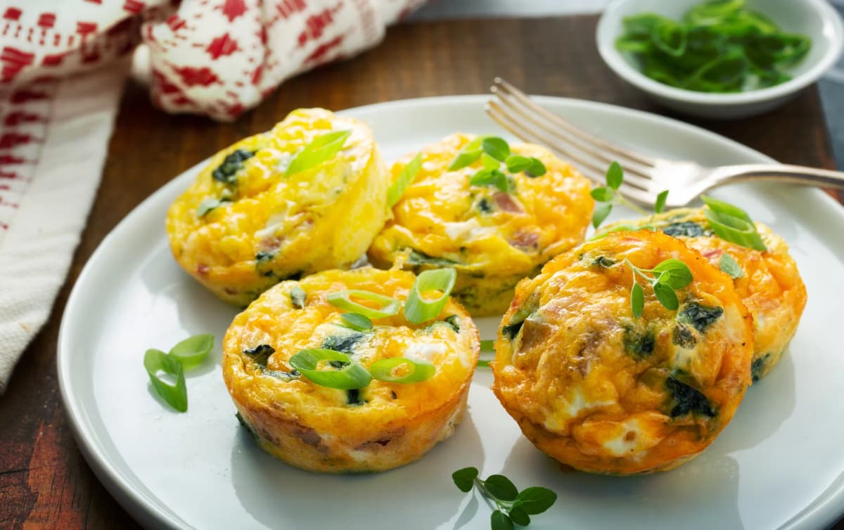 Baked egg muffins with spinach, cheese, and green onions, garnished with fresh herbs on a white plate with a fork.