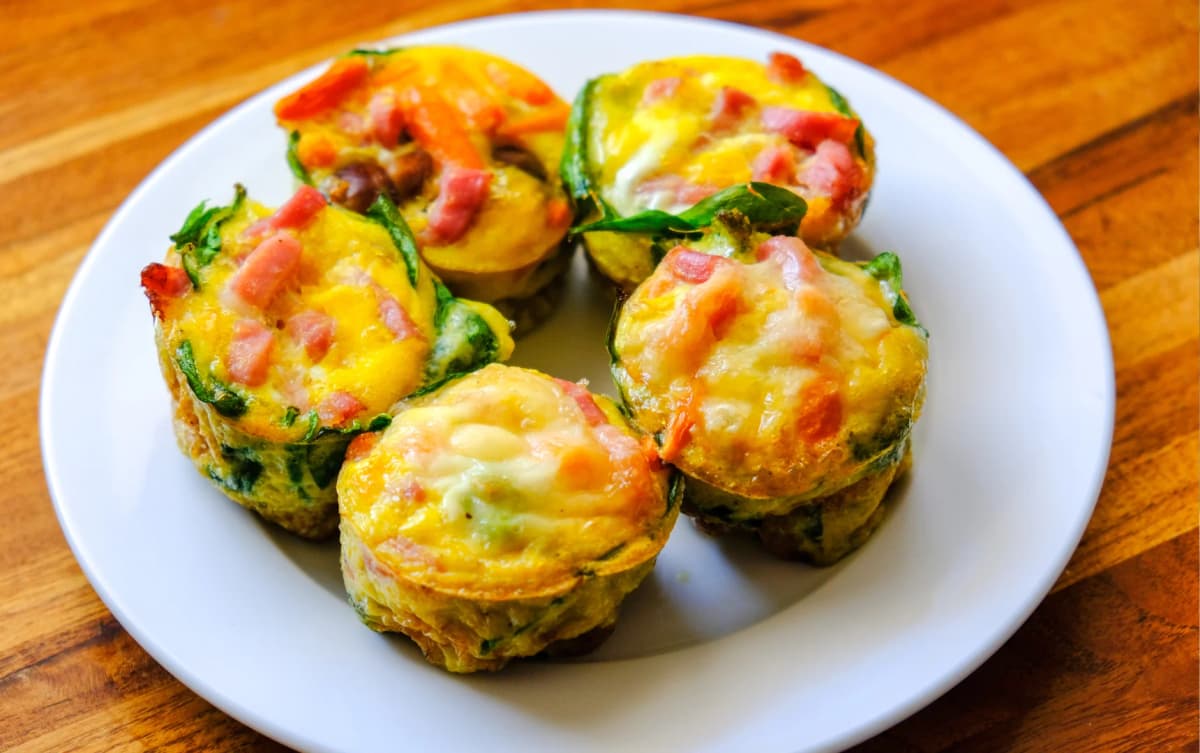 Colorful egg muffins made with spinach, ham, cheese, and vegetables, served on a white plate on a wooden table.