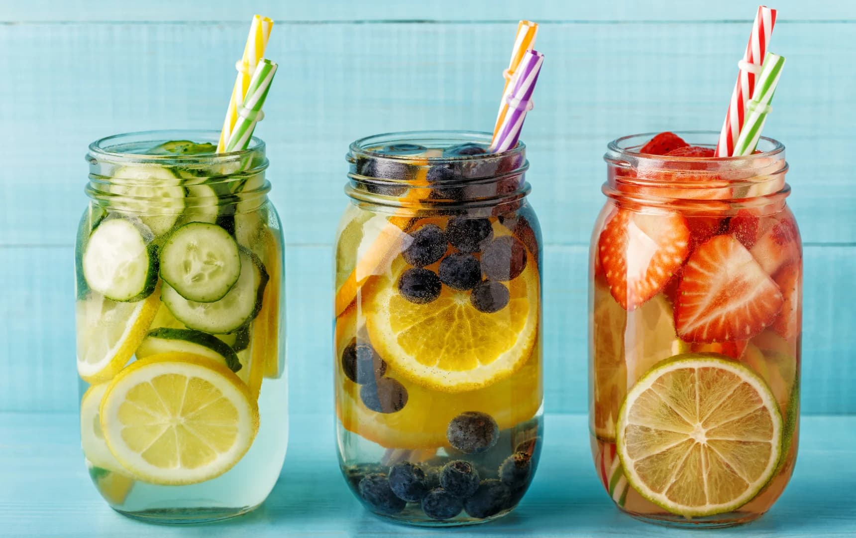Detox water jars with lemon, cucumber, blueberry, orange, strawberry, and lime slices served with colorful straws