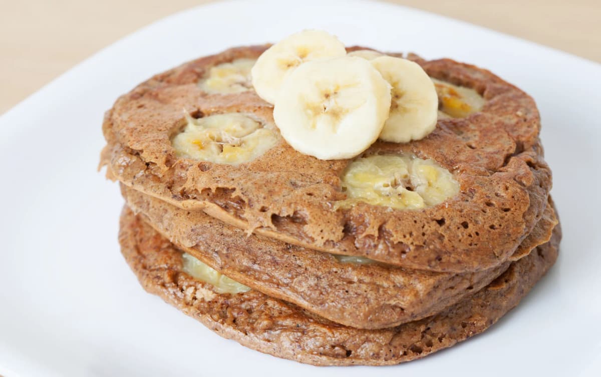 Fluffy pancakes with banana slices cooked into the batter and additional banana slices on top, served on a white plate.
