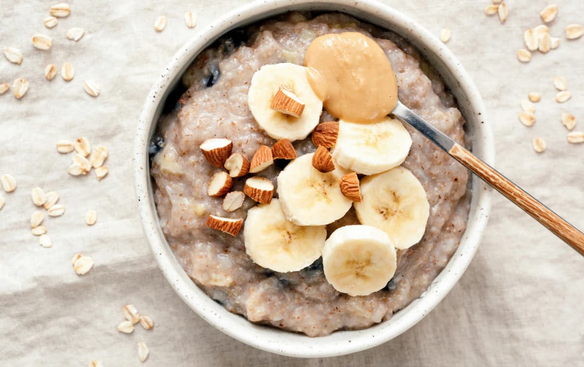 Bowl of creamy oatmeal topped with banana slices, almonds, and a spoonful of peanut butter.