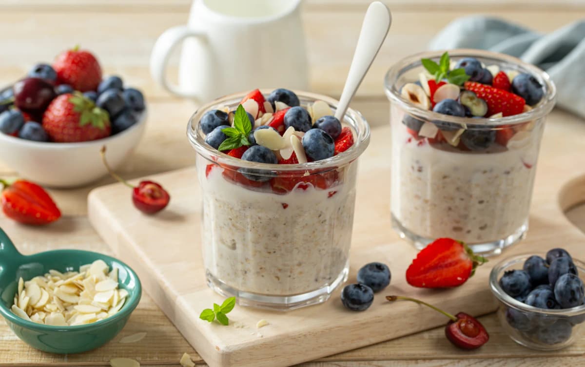 Two glass jars filled with overnight oats, topped with strawberries, blueberries, sliced almonds, and fresh mint leaves.