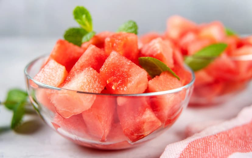 Front view of watermelon cubes in a glass jar with mint leaves garnish, and another jar of watermelon cubes in the background.
