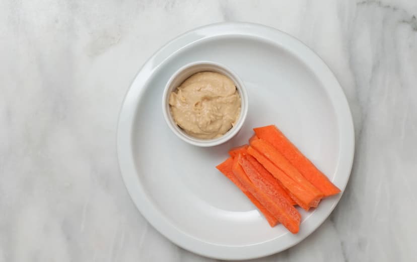 front view of carrot sticks with hummus sauce in the with dip served in white plate