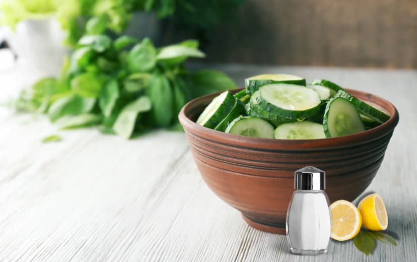 front view of cucumber slices in wooden bowl lemon slices and salt in beside bowl place in wooden table