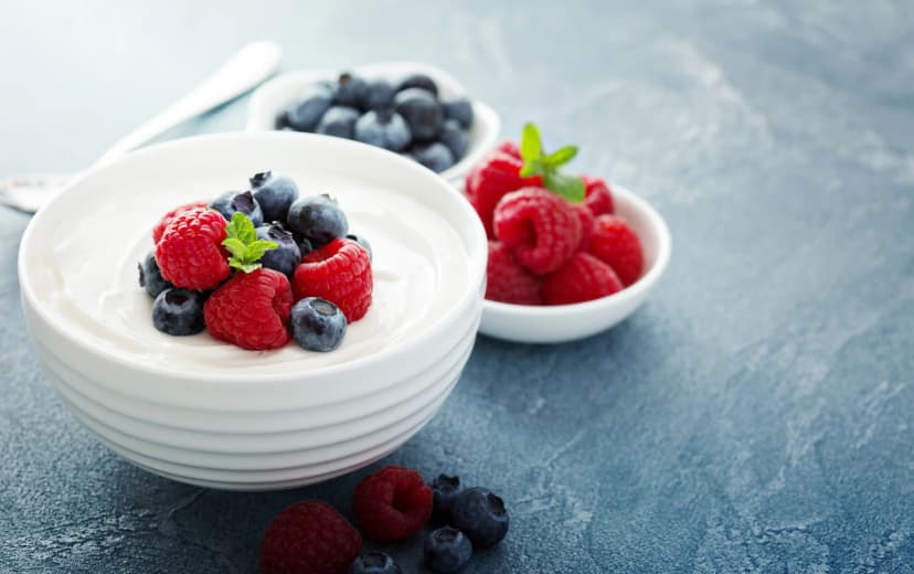 front view of greek yogurt cherry and strawberry on the top in served in white bowl also cherry and strawberry beside