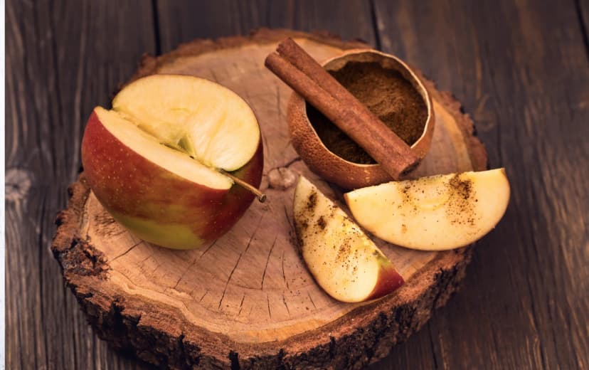 top view of cut apple and cinnamon stick and powder beside place in wooden sheet