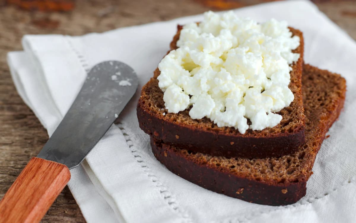 Rye bread slices topped with crumbly white cheese on a white napkin with a butter knife.
