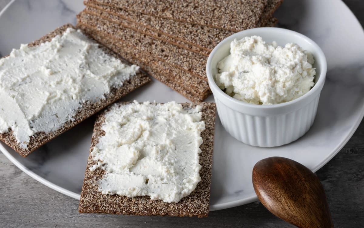 Whole grain crispbread with ricotta cheese spread and a side bowl of ricotta on a marble plate.