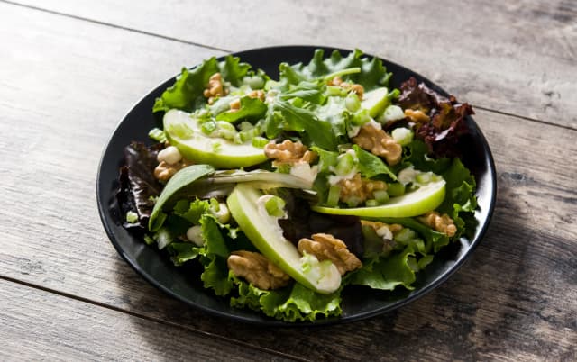 top view of spinach and green apple salad and walnuts, lettuce, served in black plate placed in wooden table