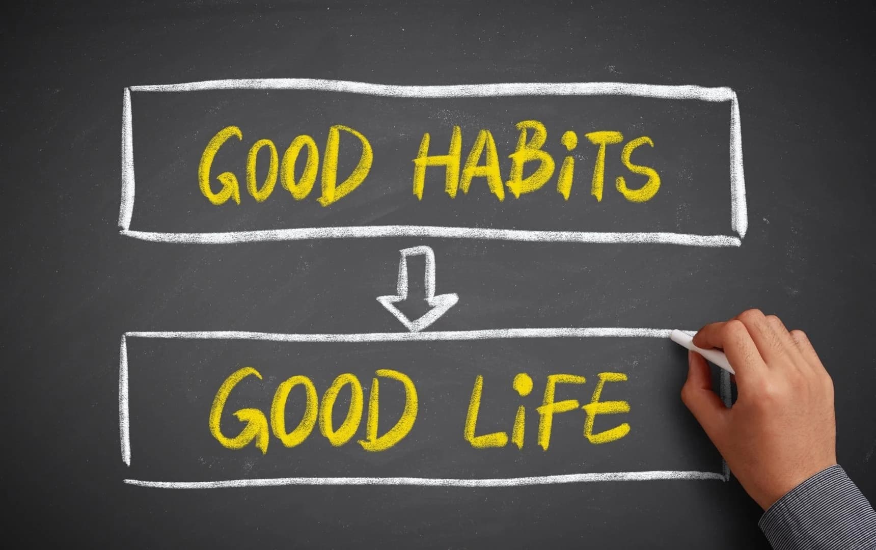 front view of a human hand writing good habits good life on black board