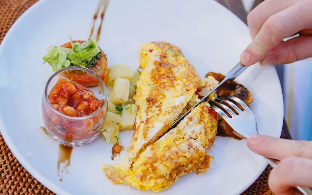 top view of a man eating egg omelette in breakfast served in white plate