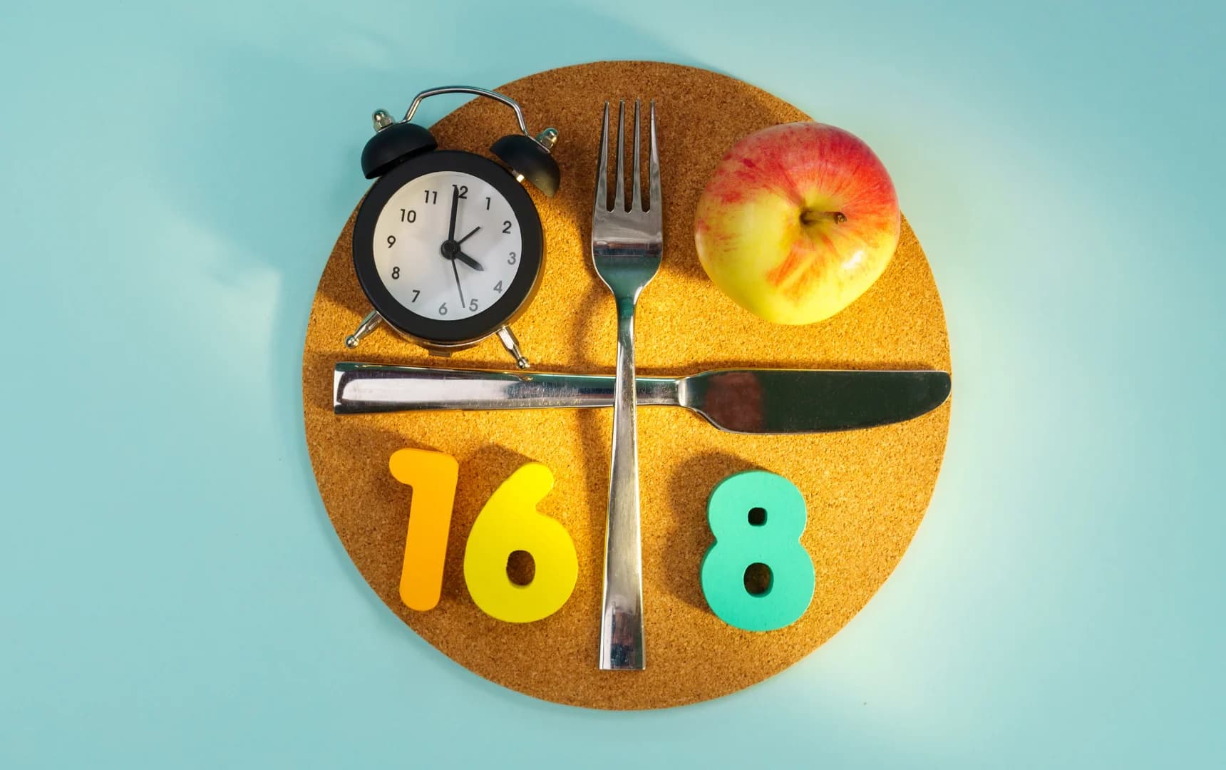 Intermittent fasting 168 method concept with clock, apple, fork and knife on cork mat