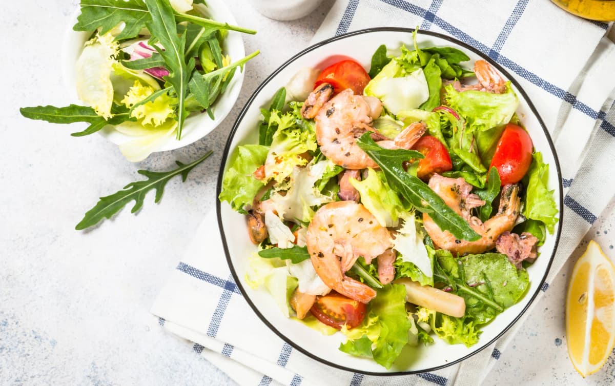 top view a healthy salad served on white bowl lemon slices and more ingredients on the background
