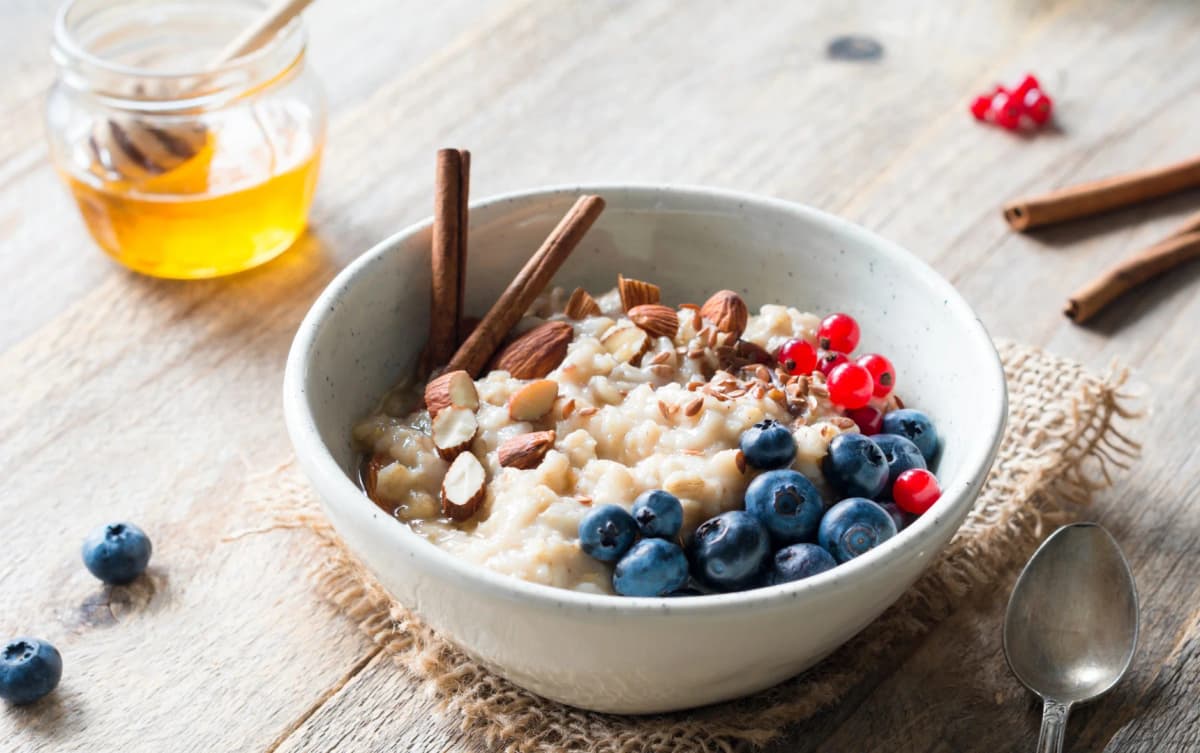 Bowl of cooked oatmeal topped with fresh blueberries, red currants, almonds, flax seeds, and cinnamon sticks