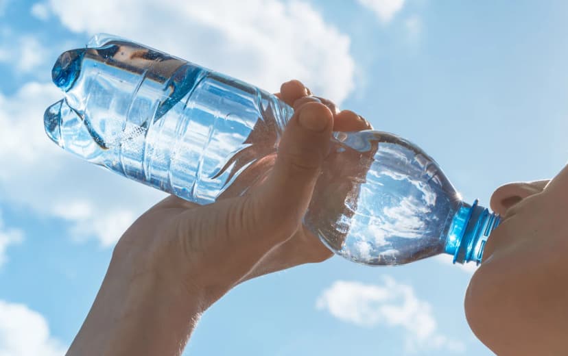 Close-up of a girl drinking from a plastic water bottle on a sunny day, with a blue sky and clouds in the background
