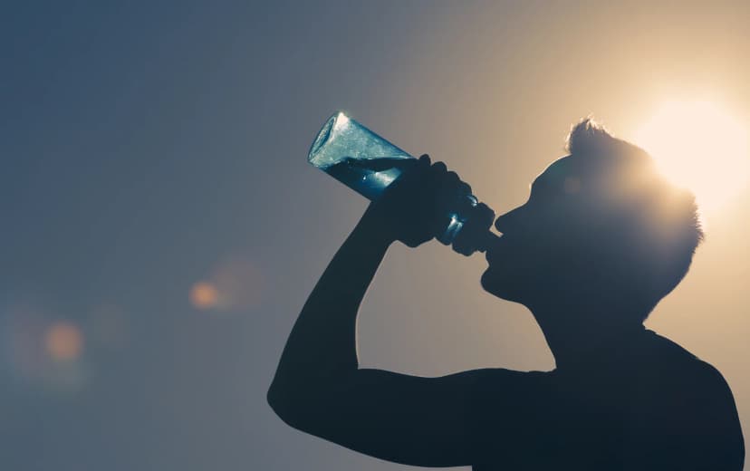 Silhouette of a man drinking from a water bottle with the sun shining behind him